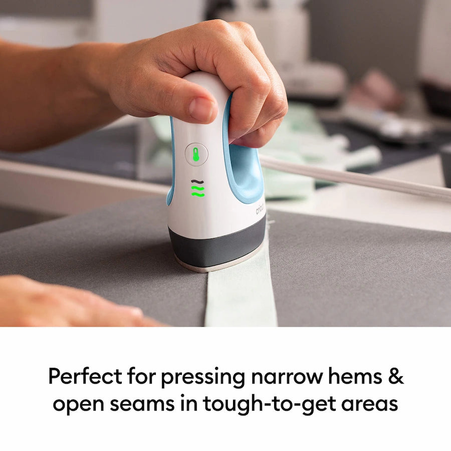 A person uses a handheld steam iron to press a gray garment on an ironing board. The iron is white with light blue accents and a dark gray base.