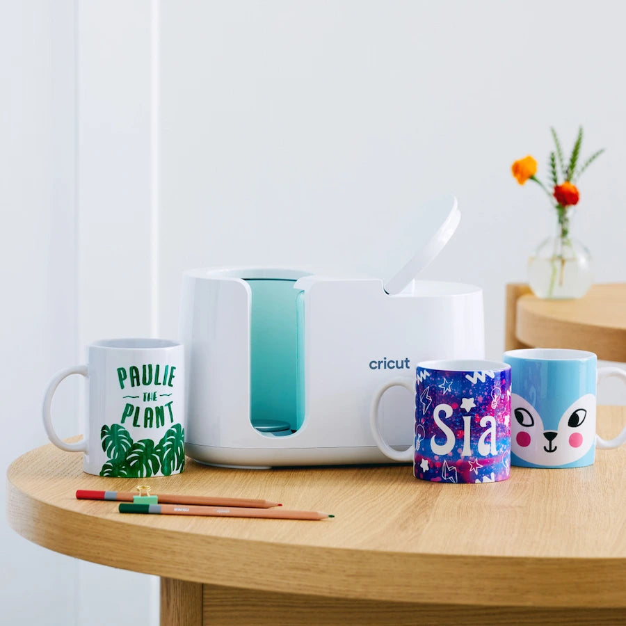 Cricut mug press with personalized mugs on a wooden table