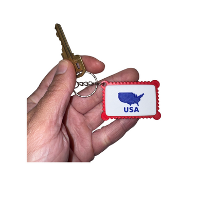 Keychain with USA map design held by a hand against a white background
