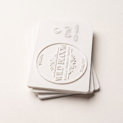 Stack of white 3D printed business cards with a raised relief logo, side-lit to show the layered texture and card edge