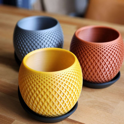 Three textured ceramic cups in yellow, gray, and red on a wooden surface.